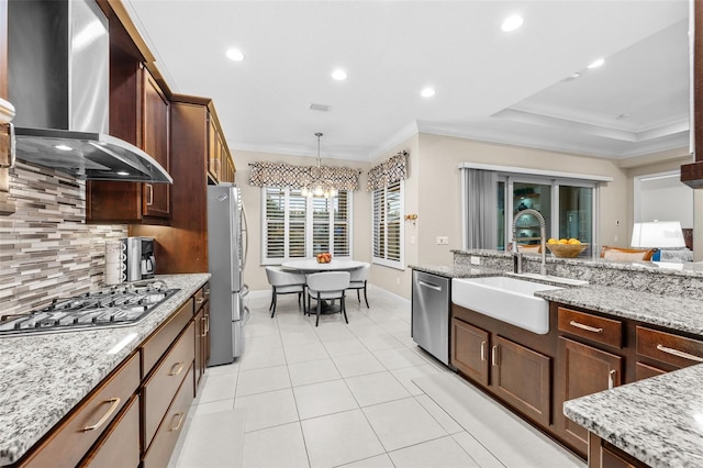 kitchen with sink, a tray ceiling, hanging light fixtures, appliances with stainless steel finishes, and wall chimney exhaust hood