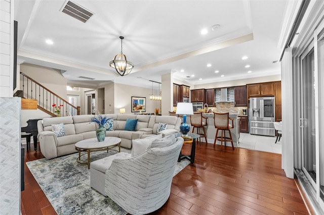 living room featuring an inviting chandelier, dark wood-type flooring, a tray ceiling, and ornamental molding