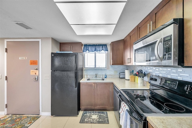 kitchen with backsplash, sink, light tile patterned floors, and black appliances