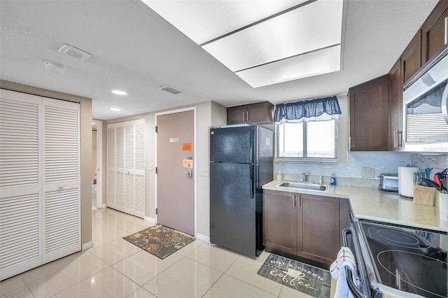 kitchen with stove, black refrigerator, sink, light tile patterned floors, and tasteful backsplash