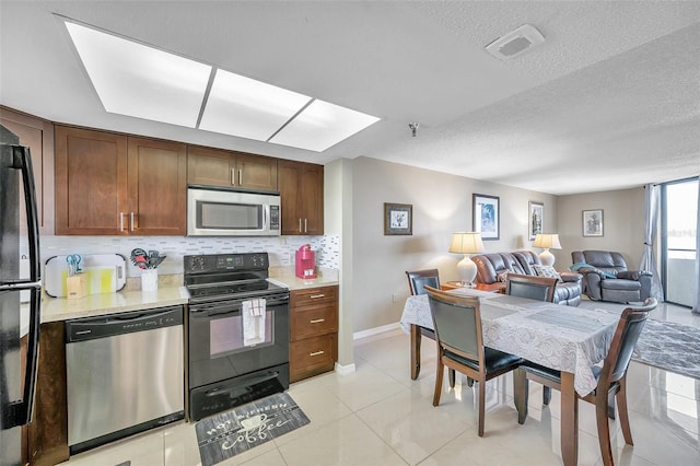 kitchen featuring backsplash, light tile patterned flooring, black appliances, and a textured ceiling