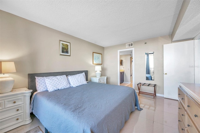 bedroom with ensuite bathroom, light tile patterned flooring, and a textured ceiling