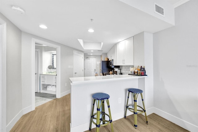 kitchen with kitchen peninsula, decorative backsplash, black fridge, light hardwood / wood-style floors, and white cabinetry