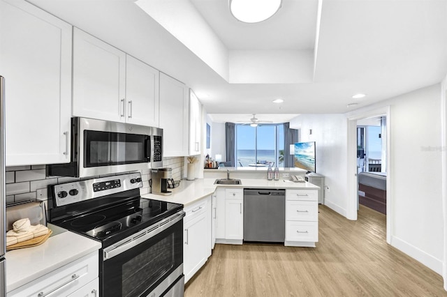 kitchen with kitchen peninsula, decorative backsplash, stainless steel appliances, sink, and white cabinetry