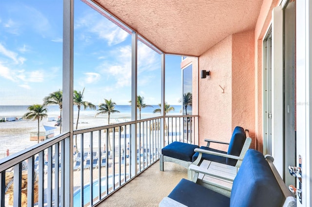 sunroom / solarium featuring a healthy amount of sunlight, a water view, and a beach view