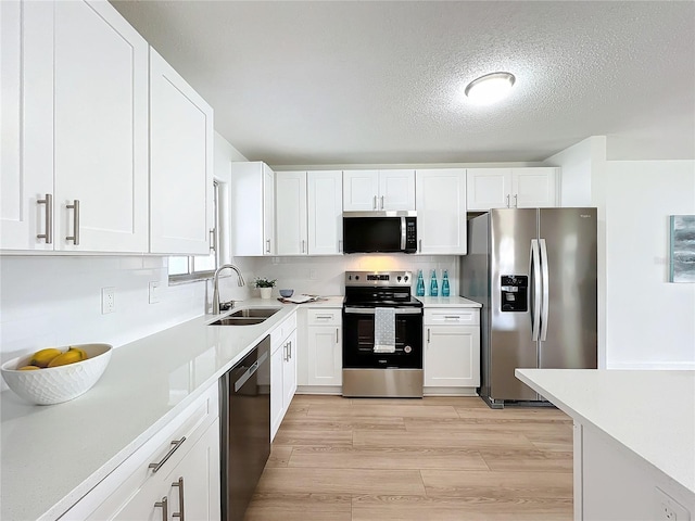 kitchen featuring appliances with stainless steel finishes, backsplash, sink, light hardwood / wood-style flooring, and white cabinetry