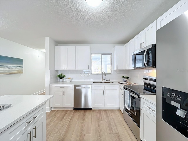 kitchen with sink, stainless steel appliances, tasteful backsplash, light hardwood / wood-style floors, and white cabinets