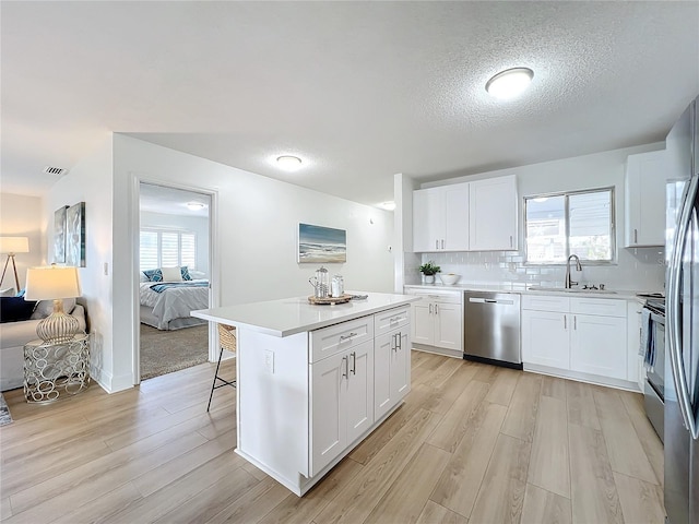 kitchen with a breakfast bar, stainless steel appliances, sink, white cabinetry, and a kitchen island