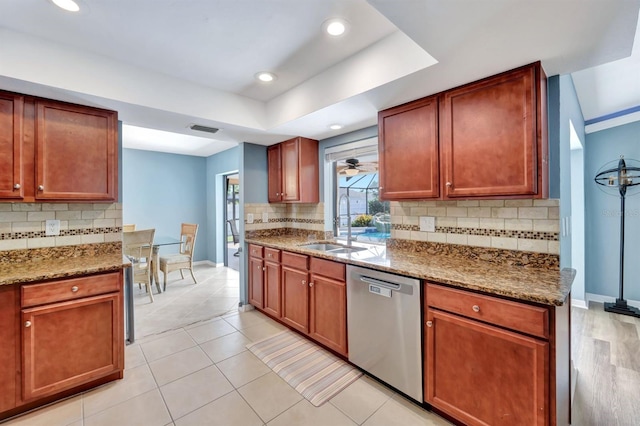 kitchen with a tray ceiling, light stone countertops, dishwasher, and sink