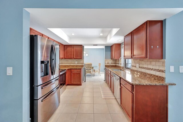 kitchen with sink, stainless steel appliances, a raised ceiling, light stone counters, and backsplash