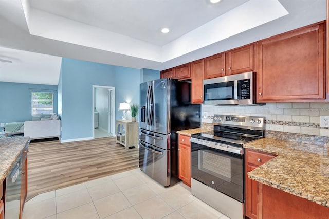 kitchen with a raised ceiling, backsplash, light stone countertops, and appliances with stainless steel finishes