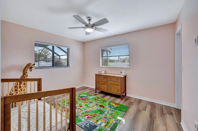 bedroom with multiple windows, light wood-type flooring, a nursery area, and ceiling fan