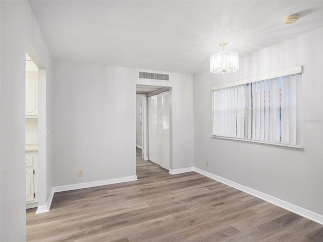 spare room with an inviting chandelier and hardwood / wood-style flooring