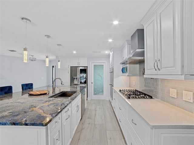 kitchen with a large island with sink, white cabinets, wall chimney range hood, sink, and stainless steel appliances