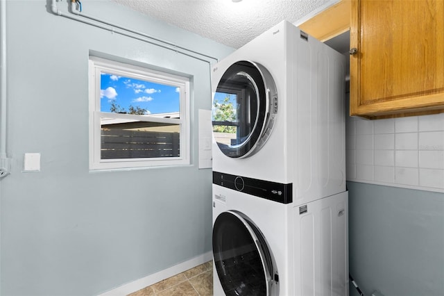 laundry area with stacked washing maching and dryer, light tile patterned floors, cabinets, and a textured ceiling