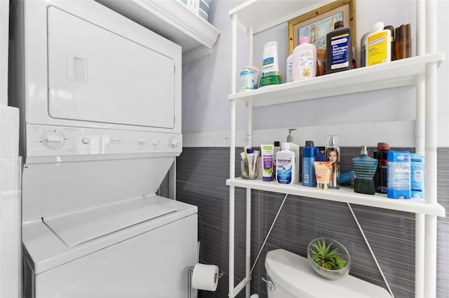 clothes washing area with stacked washing maching and dryer and tile walls