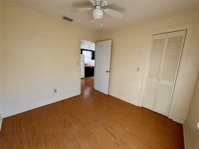 unfurnished bedroom with ceiling fan, a closet, white refrigerator, and hardwood / wood-style flooring