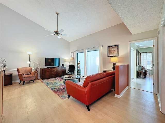 living room featuring ceiling fan, light hardwood / wood-style flooring, high vaulted ceiling, and a textured ceiling