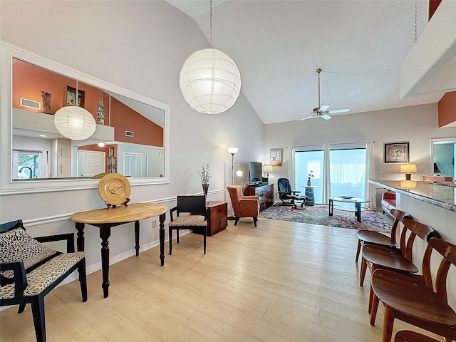 living room with a textured ceiling, light hardwood / wood-style floors, high vaulted ceiling, and ceiling fan