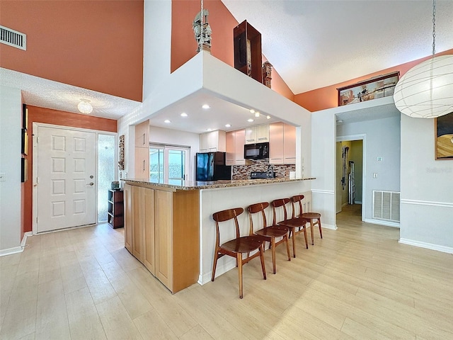 kitchen featuring stone counters, black appliances, light wood-type flooring, tasteful backsplash, and kitchen peninsula