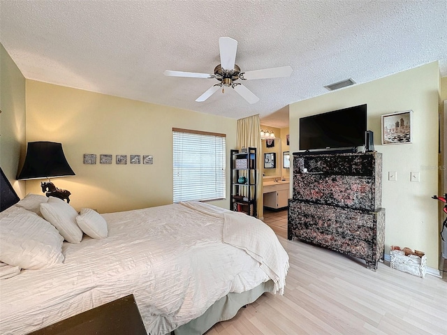 bedroom featuring ensuite bath, ceiling fan, light hardwood / wood-style flooring, and a textured ceiling