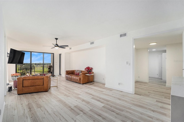 living room featuring ceiling fan, a wall of windows, and light wood-type flooring