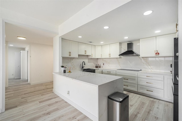 kitchen featuring kitchen peninsula, decorative backsplash, white cabinets, and wall chimney range hood