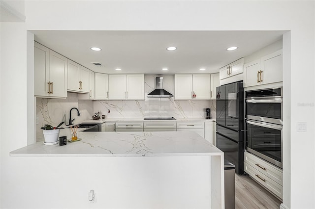 kitchen with kitchen peninsula, wall chimney exhaust hood, stainless steel double oven, sink, and white cabinetry