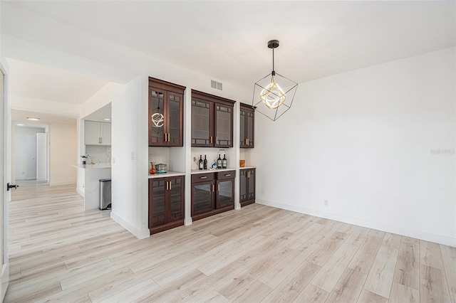 bar with decorative backsplash, dark brown cabinets, light hardwood / wood-style floors, and hanging light fixtures