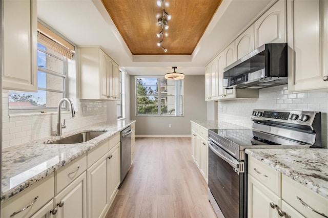 kitchen with light stone countertops, appliances with stainless steel finishes, light wood-type flooring, a raised ceiling, and sink