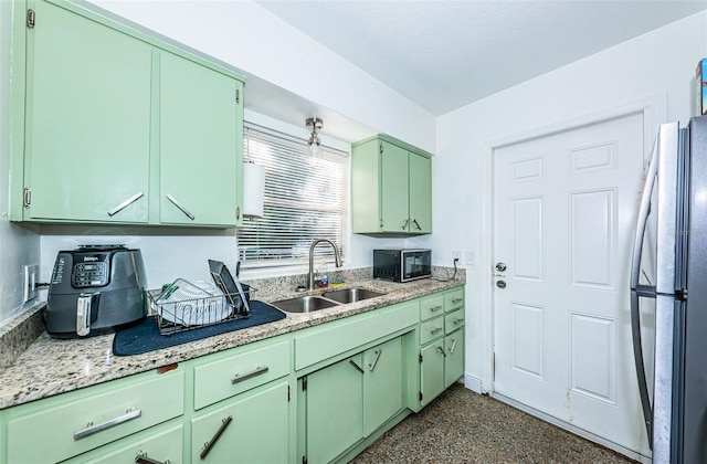 kitchen with light stone counters, stainless steel fridge, green cabinets, and sink