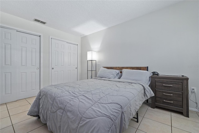 bedroom featuring light tile patterned floors, a textured ceiling, and two closets