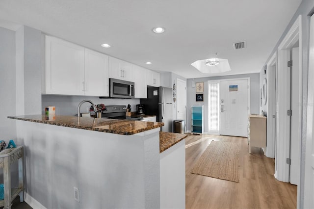 kitchen with white cabinets, kitchen peninsula, stainless steel appliances, and dark stone counters