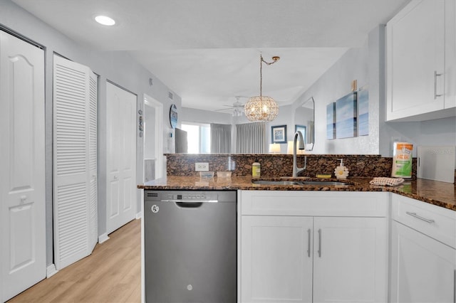 kitchen with stainless steel dishwasher, dark stone counters, sink, white cabinetry, and hanging light fixtures