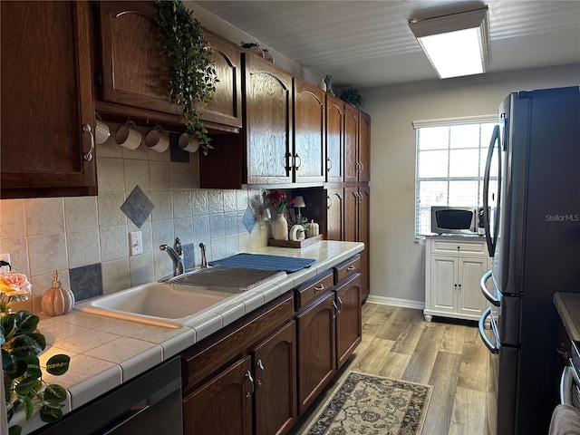 kitchen with dark brown cabinetry, dishwasher, sink, tile countertops, and refrigerator