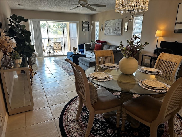 tiled dining space with a textured ceiling, plenty of natural light, and ceiling fan with notable chandelier