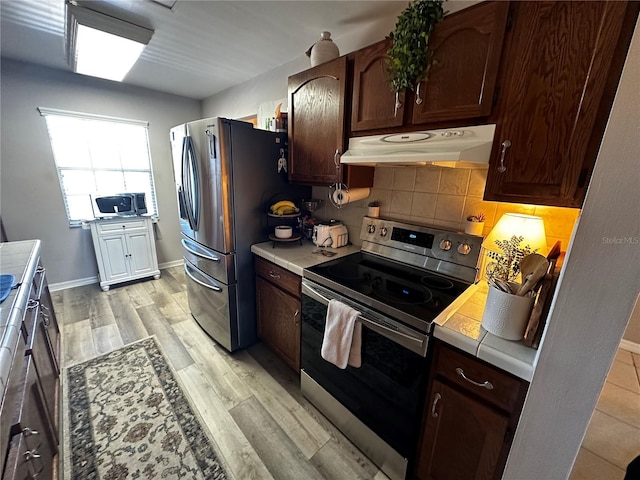 kitchen with tile countertops, tasteful backsplash, light hardwood / wood-style floors, dark brown cabinetry, and stainless steel appliances