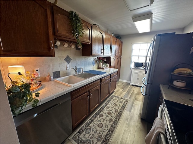 kitchen featuring sink, stainless steel appliances, backsplash, tile countertops, and light wood-type flooring