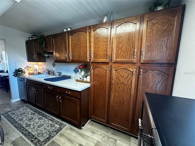 kitchen with light wood-type flooring, backsplash, stainless steel dishwasher, sink, and tile countertops