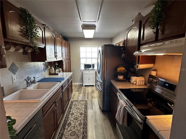 kitchen with tile countertops, sink, light hardwood / wood-style flooring, dark brown cabinetry, and stainless steel appliances