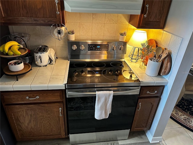 kitchen with tile counters, stainless steel range, backsplash, extractor fan, and dark brown cabinets