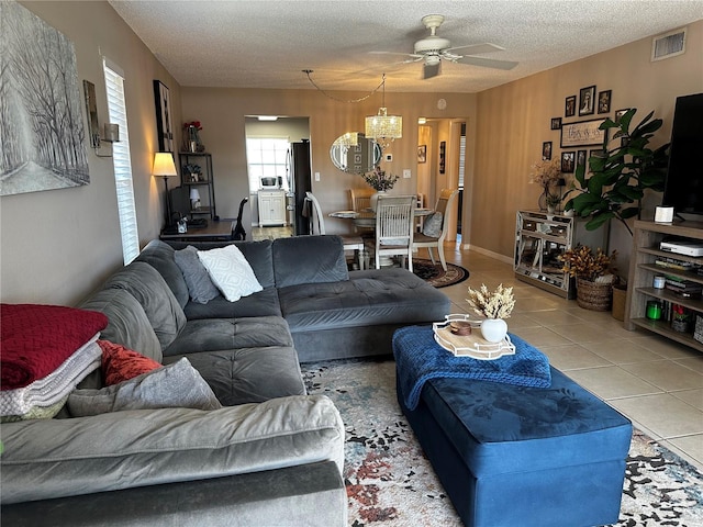 tiled living room with ceiling fan with notable chandelier and a textured ceiling