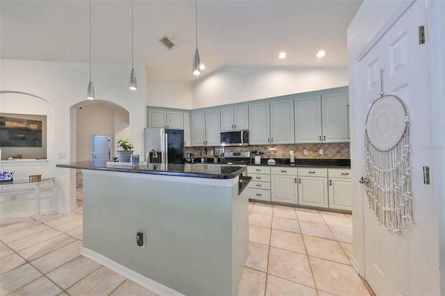 kitchen featuring appliances with stainless steel finishes, tasteful backsplash, pendant lighting, light tile patterned floors, and a center island with sink