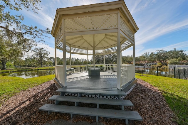 wooden terrace featuring a gazebo, a water view, and a lawn