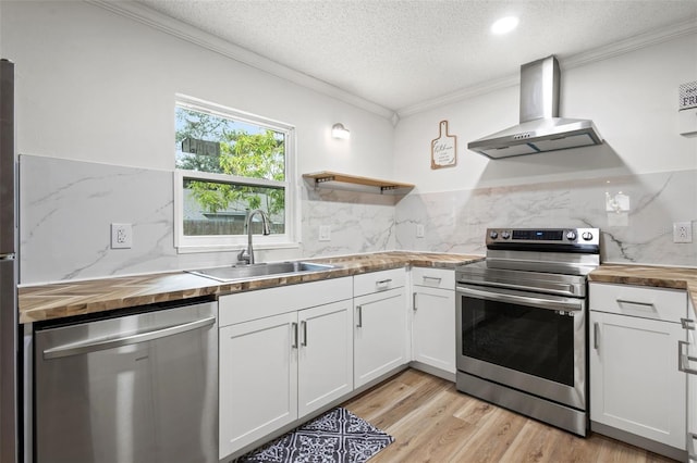 kitchen with wall chimney range hood, wood counters, appliances with stainless steel finishes, and white cabinetry