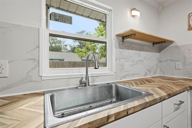 kitchen with butcher block countertops, a sink, white cabinetry, backsplash, and open shelves