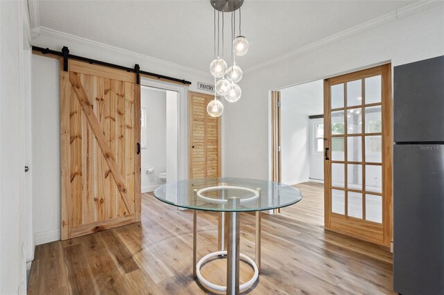 unfurnished dining area featuring a barn door, baseboards, visible vents, wood finished floors, and crown molding