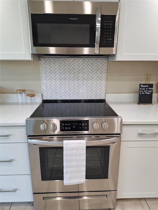 kitchen with light tile patterned flooring, light stone countertops, white cabinetry, and stainless steel appliances