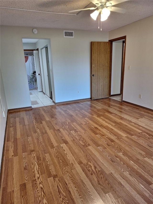 unfurnished room with ceiling fan, light wood-type flooring, and a textured ceiling