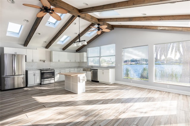 kitchen with ceiling fan, a center island, stainless steel appliances, vaulted ceiling with skylight, and white cabinets